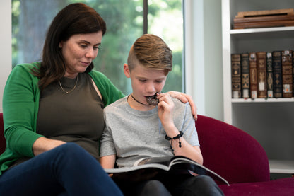 Mom and son reading while boy chews on brown donut chewelry.