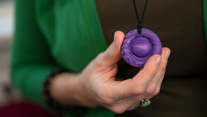 Adult female hand holding her pop it chew necklace in wavy purple.