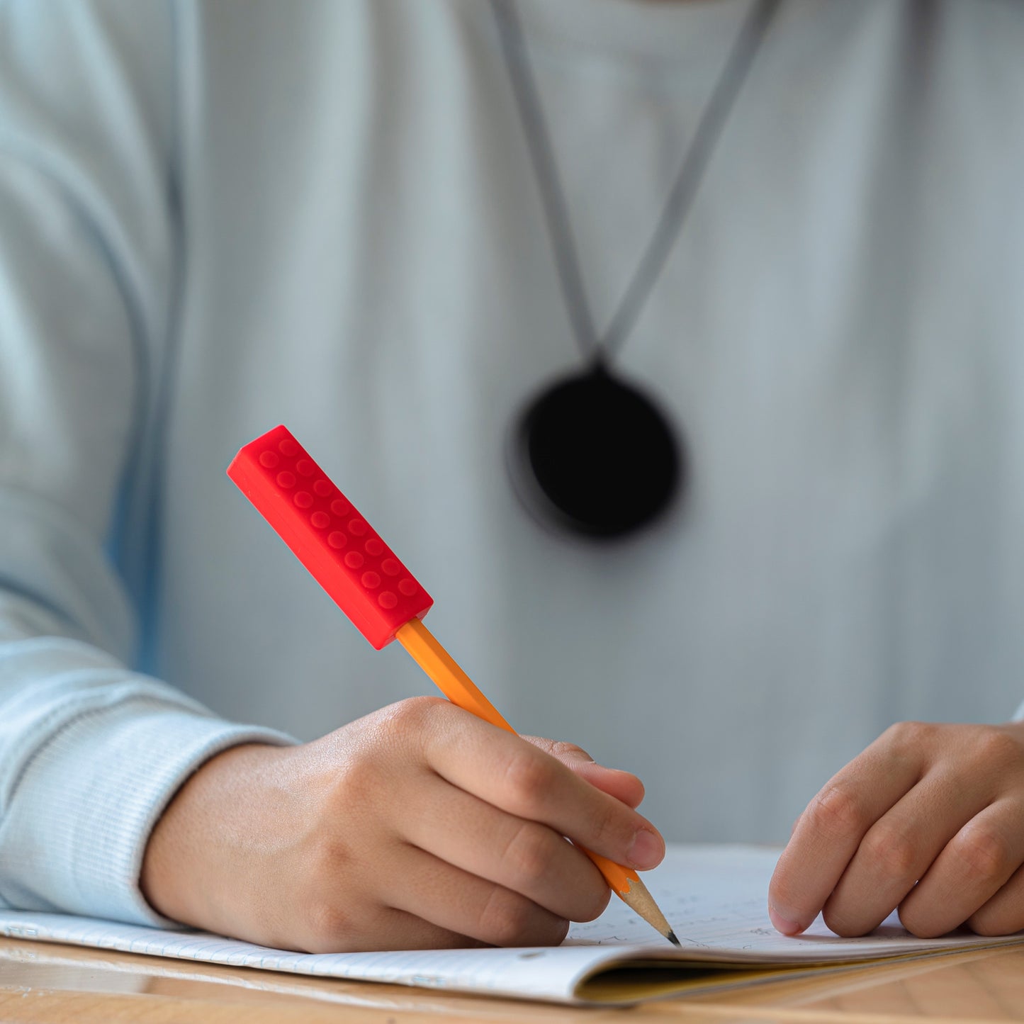 Teen girl uses pencil with red Chew Blockz Chewable Pencil Topper