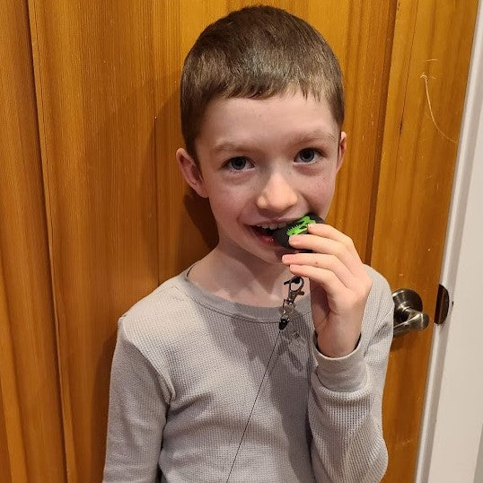 Boy chews on dinosaur skull chewelry attached to retractable lanyard.