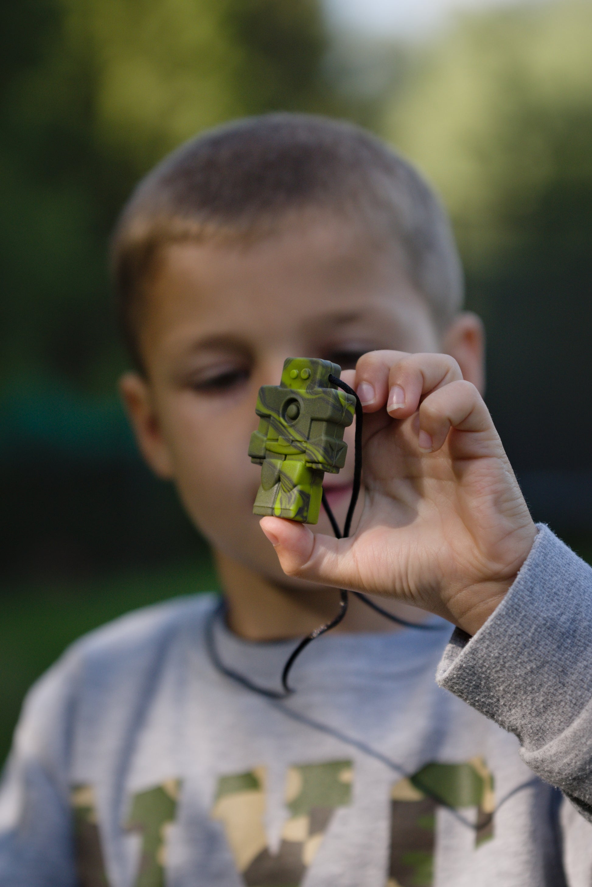 Boy holds green camo robot chew necklace